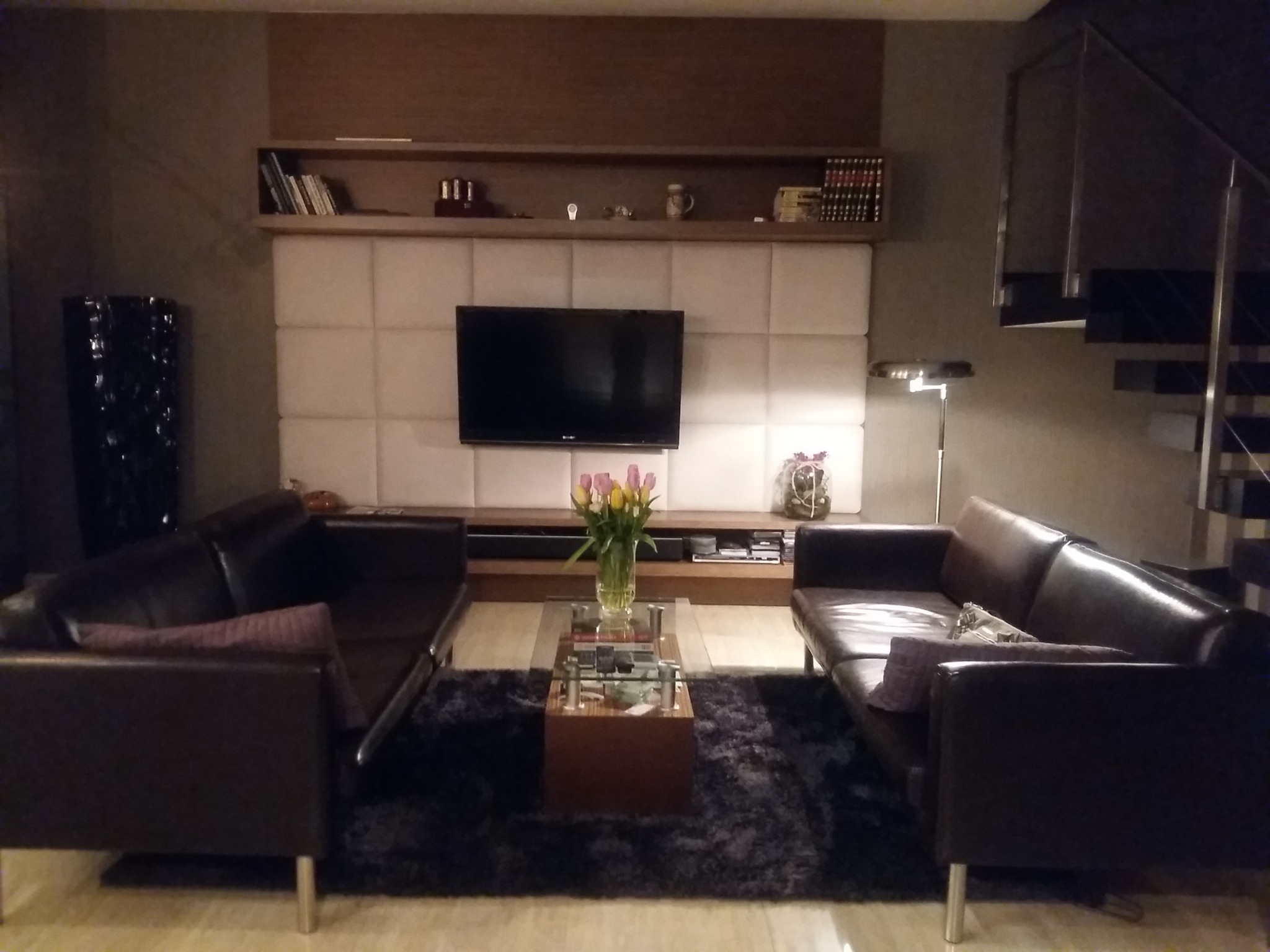 Salon z dwiema skórzanymi sofami w odcieniach brązu, stolikiem kawowym z kwiatami i ścianą z panelem tapicerowanym za telewizorem.