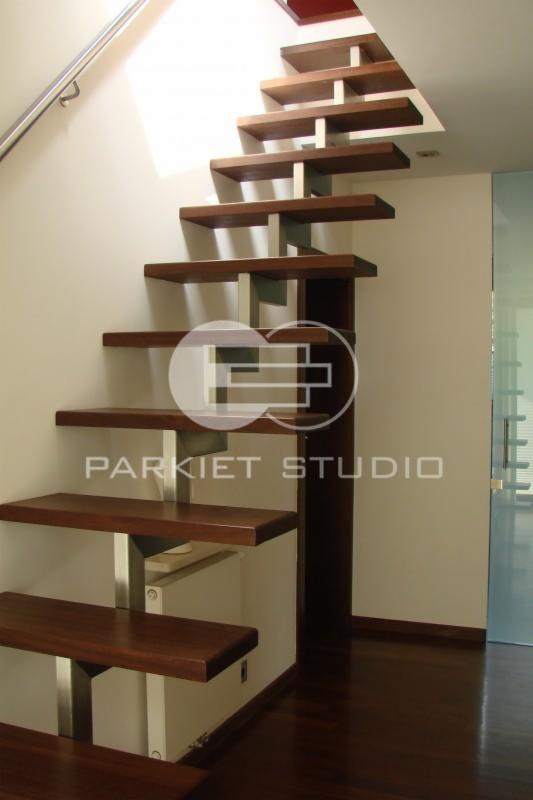 Nowoczesne schody wspornikowe z ciemnego drewna i metalowymi wspornikami, oświetlone światłem wpadającym z góry.