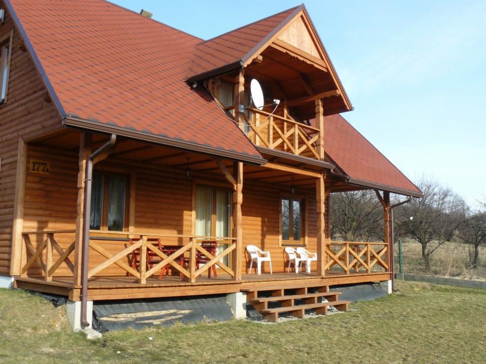 Dwukondygnacyjny dom z bali z czerwonym dachem, balkonem z satelitą i zadaszonym tarasem z drewnianymi balustradami.