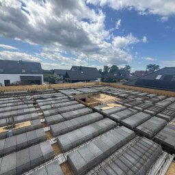 E&D HOUSE SPÓŁKA Z OGRANICZONĄ ODPOWIEDZIALNOŚCIĄ - Żórawina: Zbrojenie stropu Teriva na budowie domu jednorodzinnego. Widoczne pustaki szalunkowe i stalowe pręty zbrojeniowe na tle nieba.