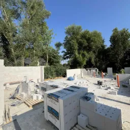 Budowa domu z bloczków silikatowych SIL-PRO, Wrocław Jarnołtów. Częściowo wzniesione ściany, palety z materiałem budowlanym na placu budowy w słoneczny dzień.