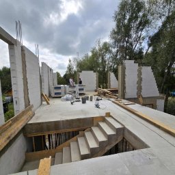 E&D HOUSE SPÓŁKA Z OGRANICZONĄ ODPOWIEDZIALNOŚCIĄ - Budowa domu z betonu komórkowego: widok na wznoszone ściany z betonu komórkowego, zbrojenie i betonowe schody w surowym stanie. W tle widoczni pracownicy.