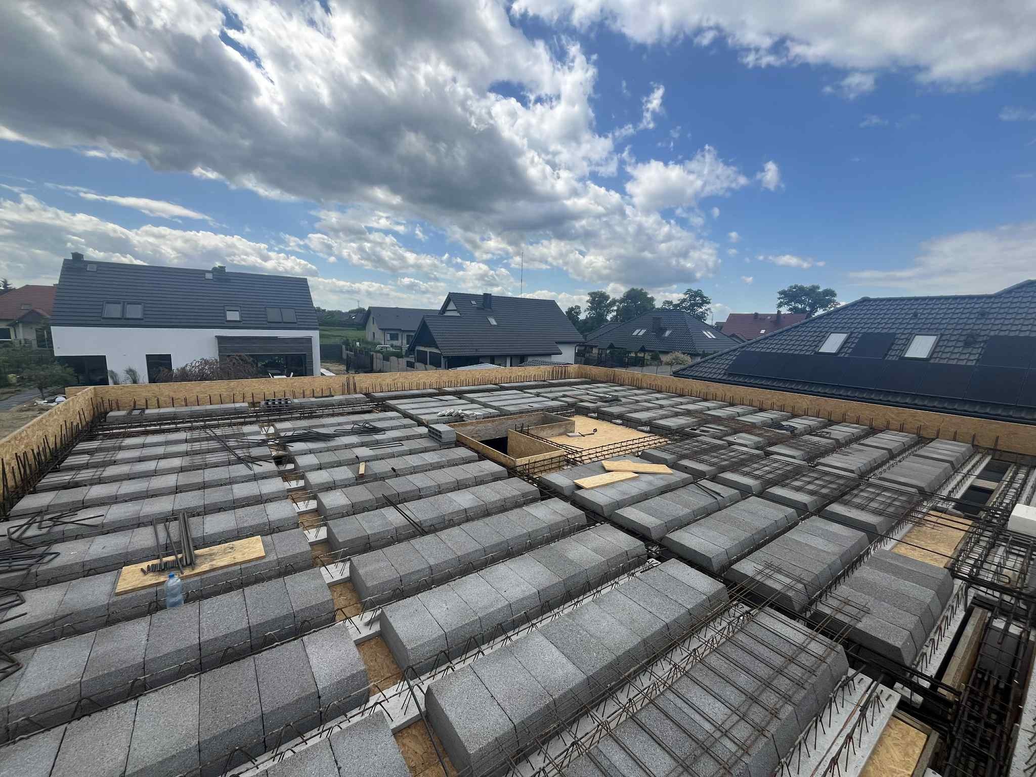 Żórawina: Zbrojenie stropu Teriva na budowie domu jednorodzinnego. Widoczne pustaki szalunkowe i stalowe pręty zbrojeniowe na tle nieba.