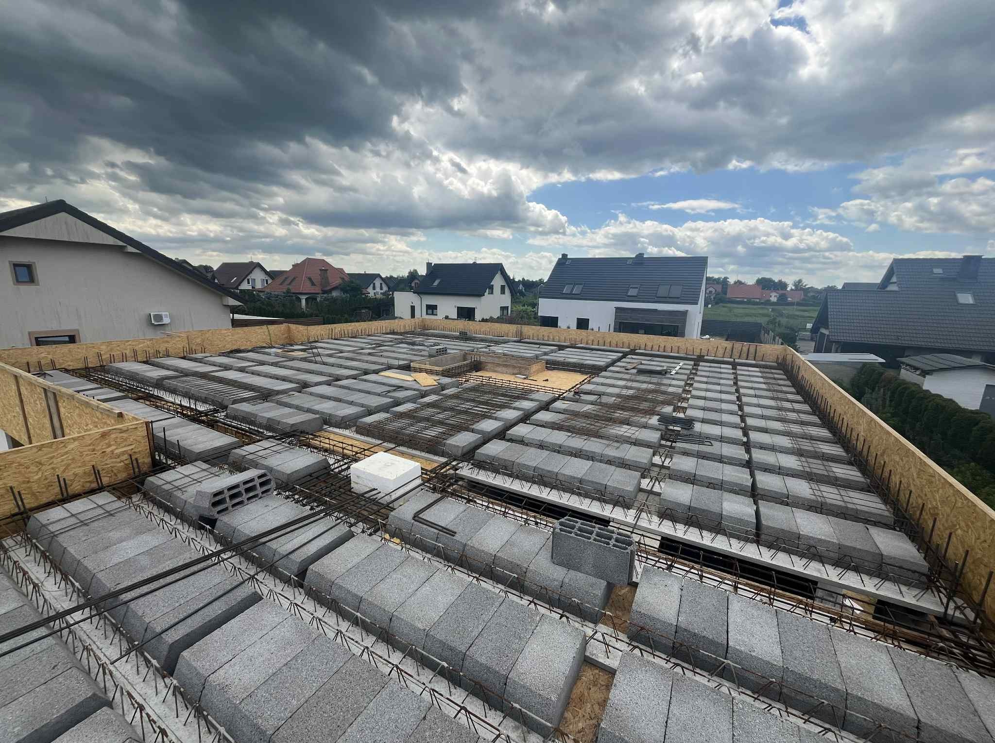 Żórawina: strop Teriva z betonowymi pustakami i zbrojeniem, widok z góry na tle pochmurnego nieba i zabudowy jednorodzinnej, szalunek krawędziowy z desek.