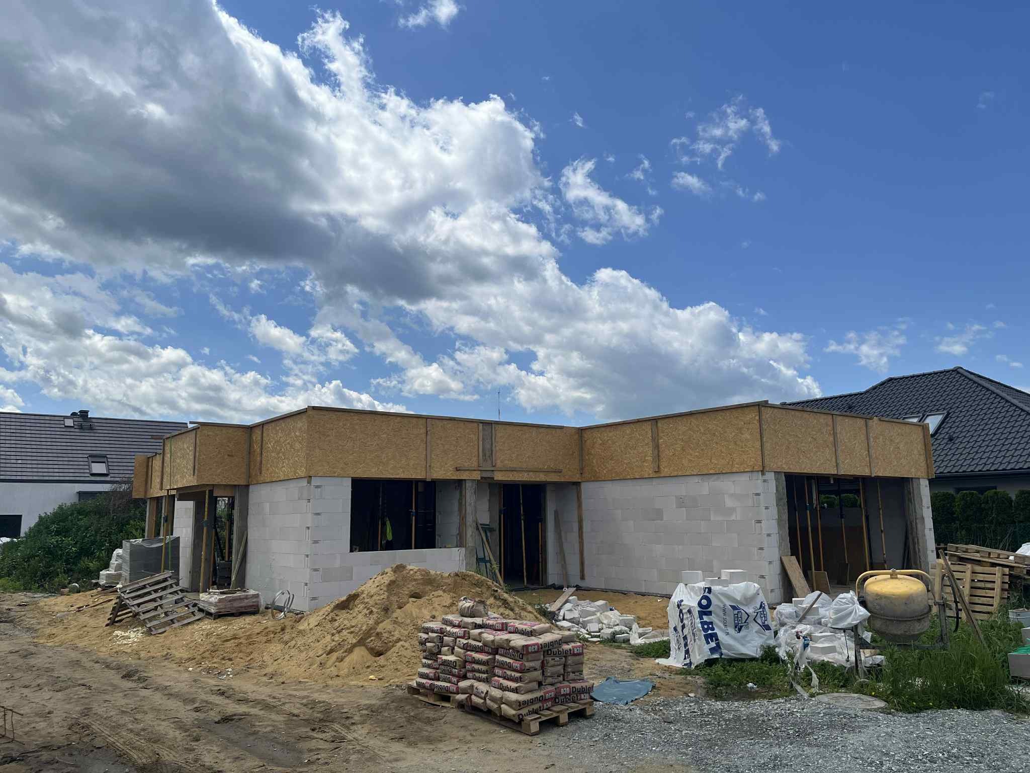 Budowa domu jednorodzinnego w Żórawinie: ściany z betonu komórkowego Solbet, widoczne worki z zaprawą, drewniane elementy szalunku i błękitne niebo z chmurami.