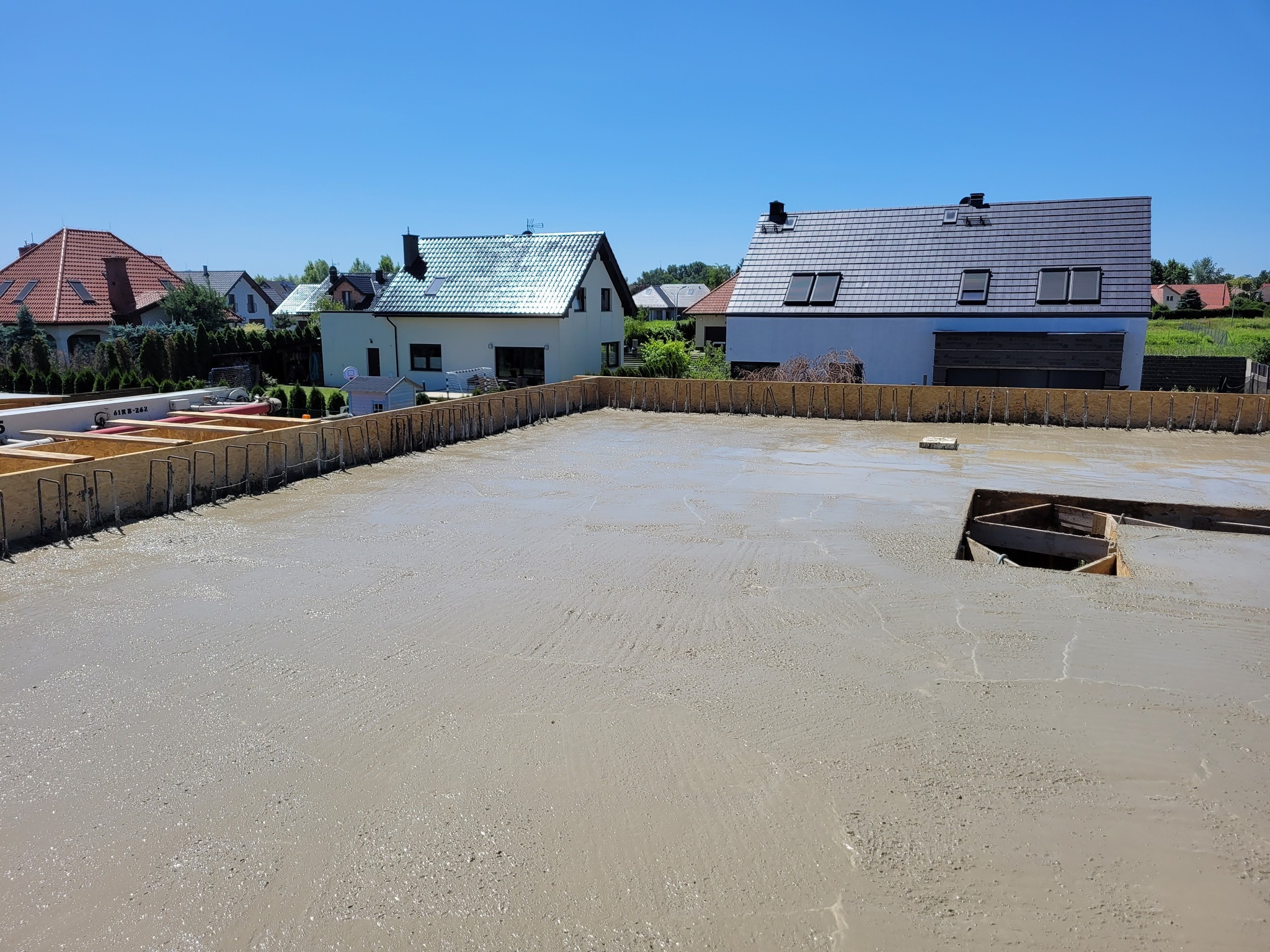 Wylany fundament pod budowę domu w Żórawinie. Widoczne szalunki i zbrojenie. W tle zabudowa jednorodzinna w słoneczny dzień.