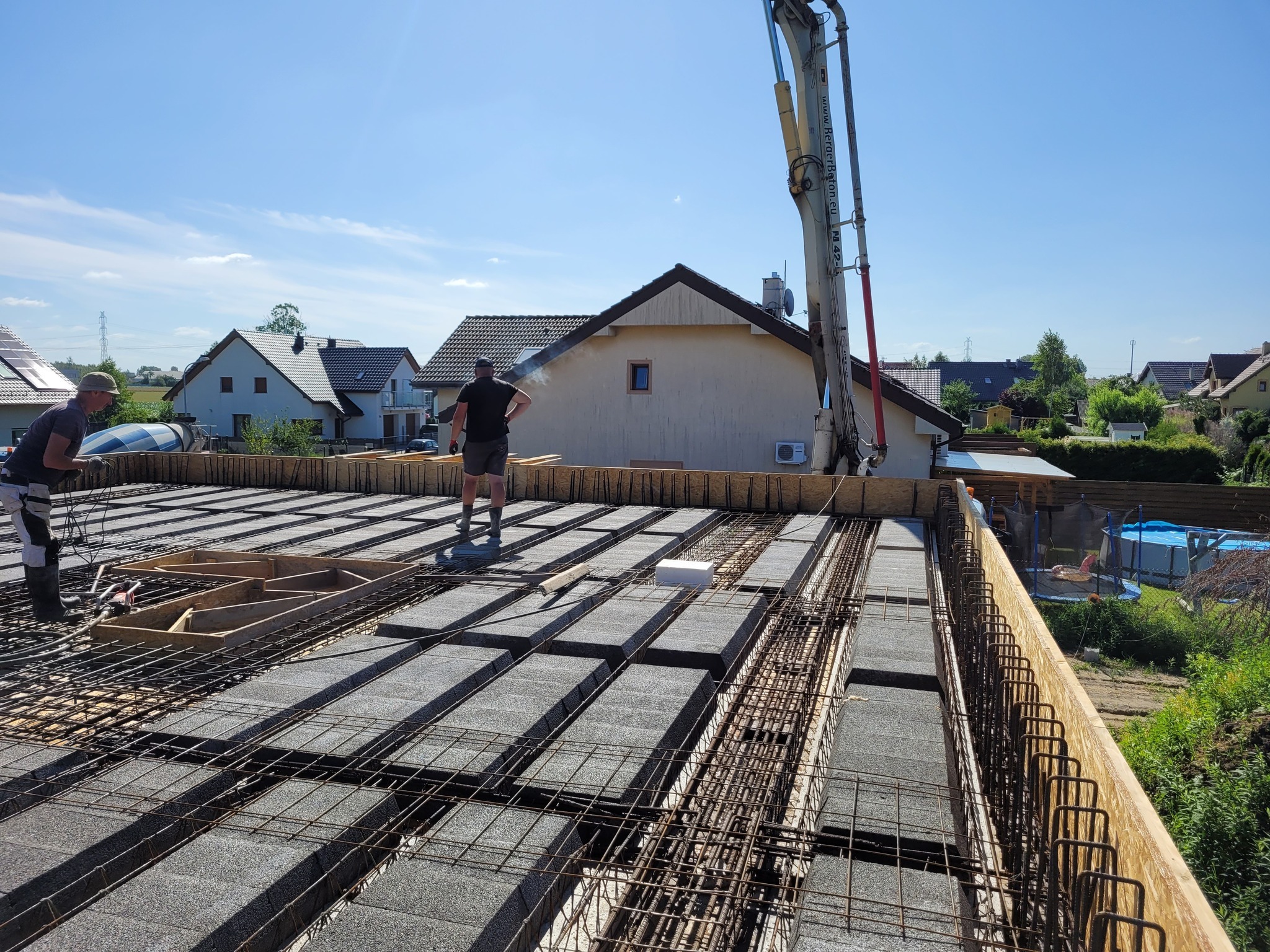 Budowa stropu Teriva: szalunek, betonowe bloczki i zbrojenie na tle domów jednorodzinnych i nieba. W tle pompa do betonu. Żórawina.