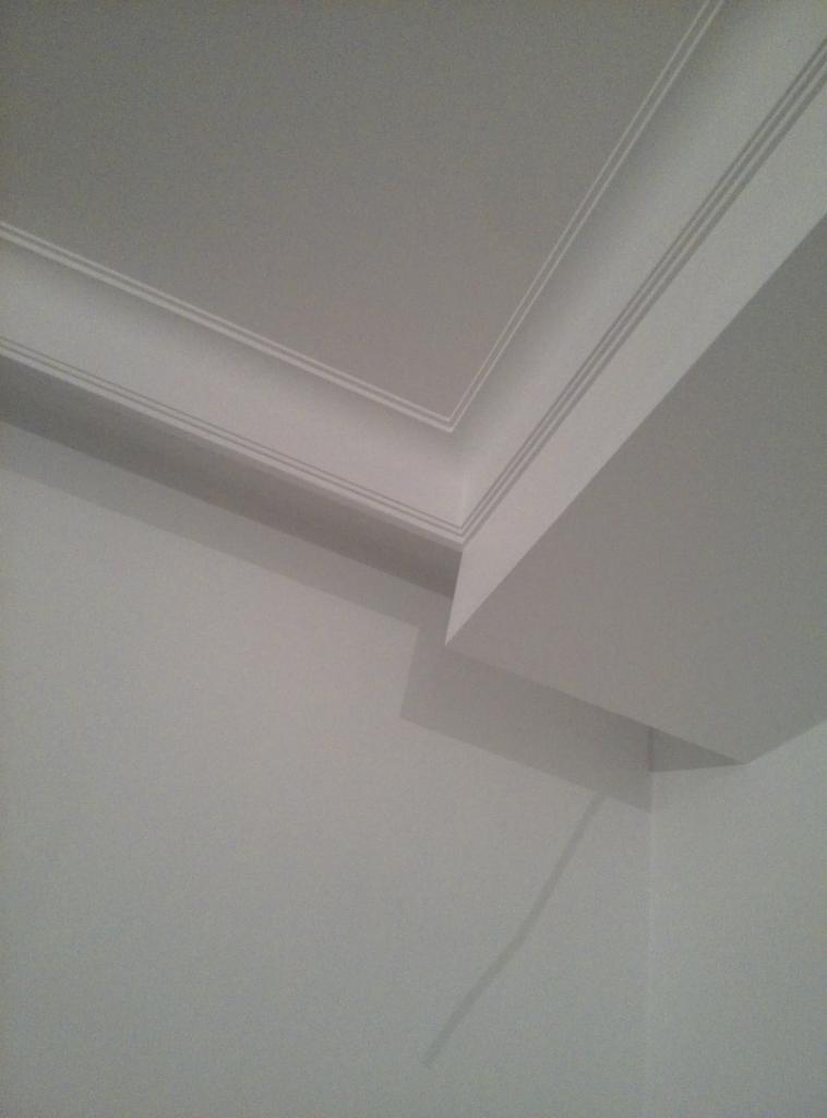Szare wnętrze z wykończonym sufitem i ścianami, widoczne listwy dekoracyjne na styku sufitu i ścian.