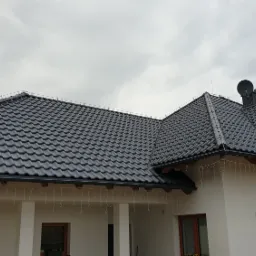 Nowoczesny dom jednorodzinny z grafitowym dachem z dachówki ceramicznej, widoczne rynny i komin z anteną satelitarną, ozdobiony świątecznymi lampkami.