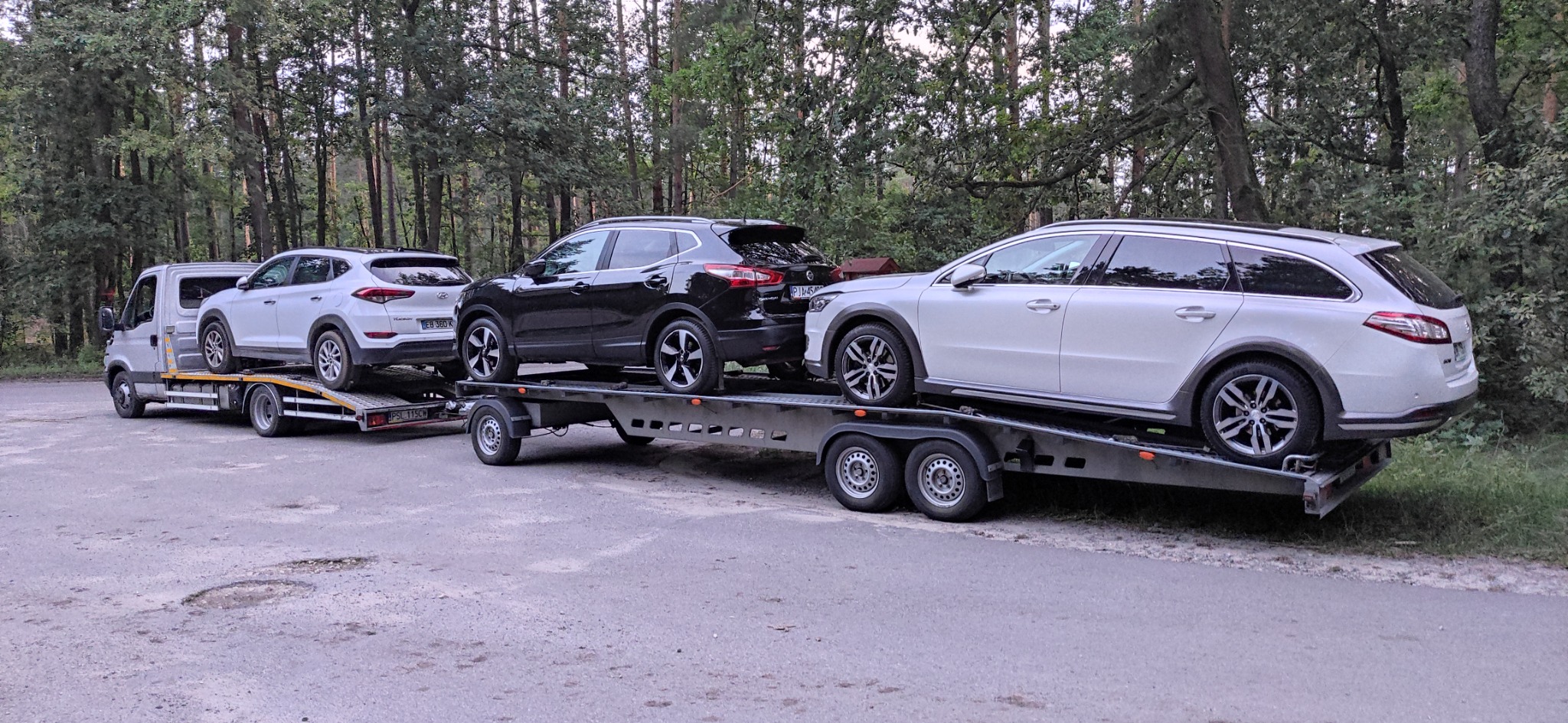 Laweta z trzema samochodami osobowymi: białym Hyundai Tucson, czarnym Nissan Qashqai i białym Peugeot 508 kombi, na tle lasu.