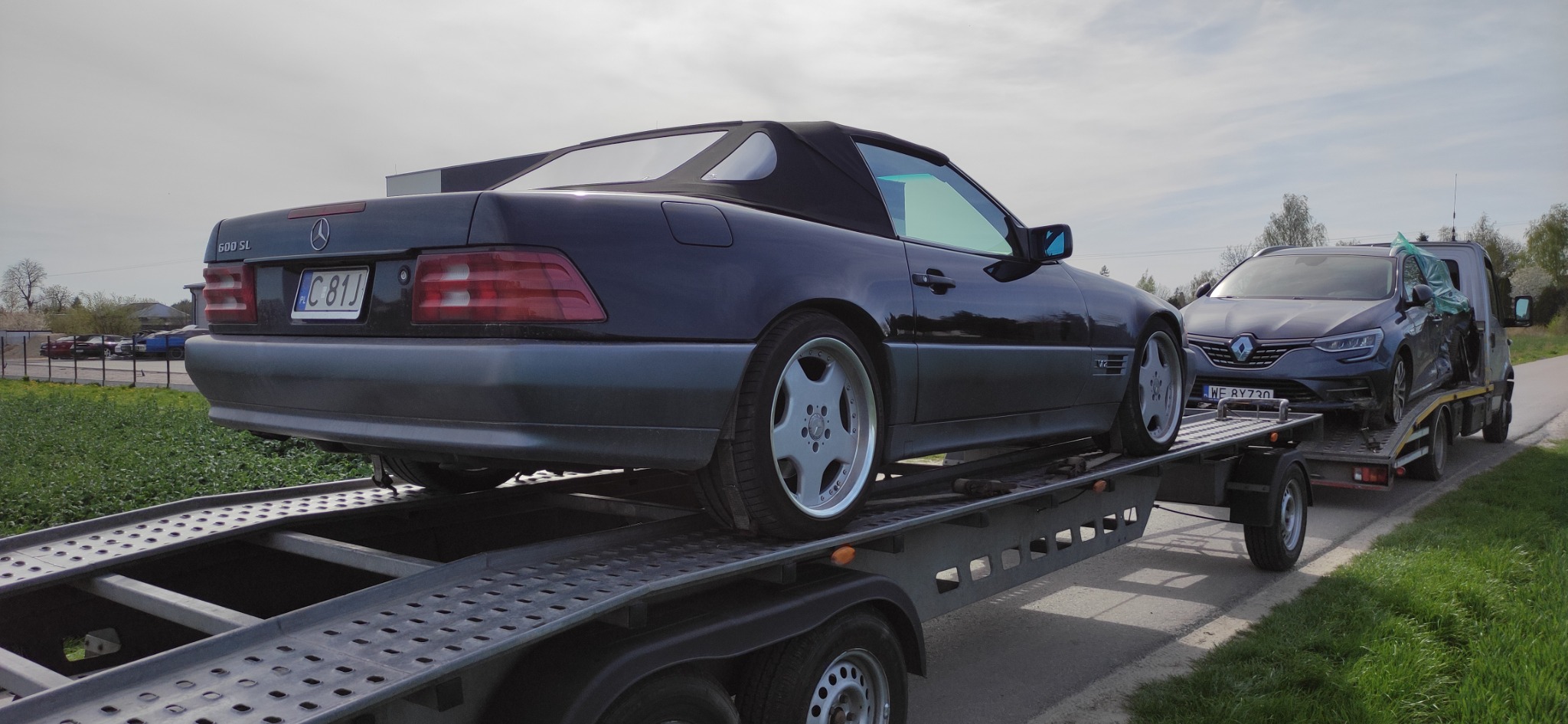 Czarny Mercedes SL 600 na lawecie, za nim uszkodzony Renault Megane, transport dwóch aut jednocześnie.