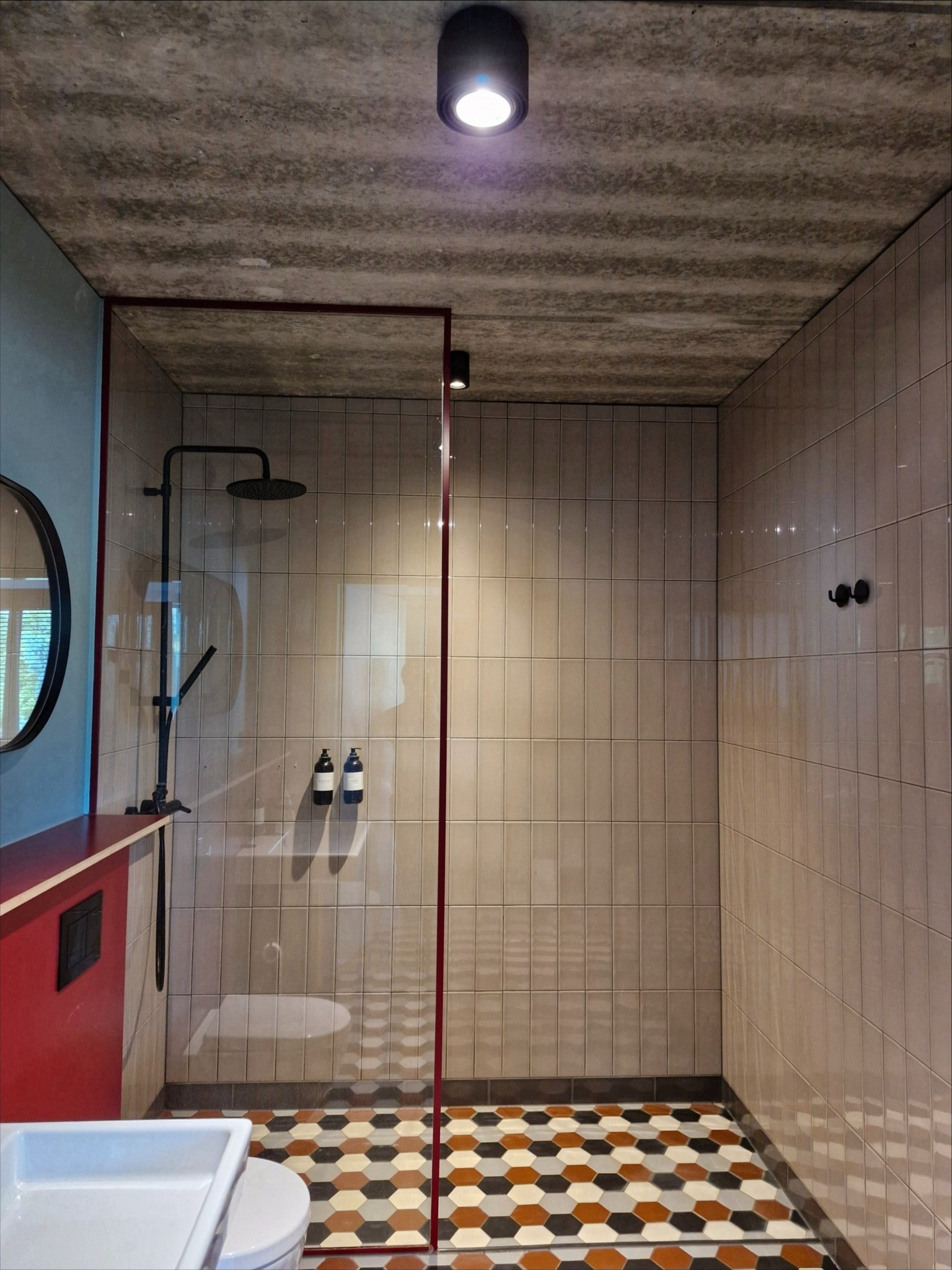 Wykończona łazienka z kabiną prysznicową typu walk-in, beżowymi płytkami ściennymi, heksagonalną mozaiką podłogową i elementami w kolorze czerwonym.