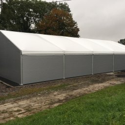 Przedsiębiorstwo Usług Produkcji i Handlu ECOPOL Ireneusz Zioła - Gotowa hala z płyt warstwowych, szara elewacja, biały dach, widok z zewnątrz, teren zielony, pochmurne niebo. Widoczna drabina oparta o ścianę.