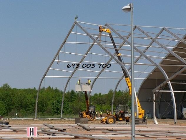 Wznoszenie szkieletu hali namiotowej z użyciem podnośników koszowych, widoczne stalowe elementy konstrukcyjne oraz przygotowane podłoże z oznaczeniem strefy 'H'.