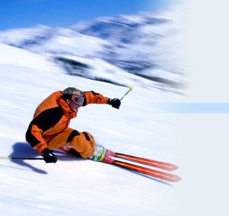 Narciarz w pomarańczowym kombinezonie zjeżdża po ośnieżonym stoku górskim, widoczny w ruchu z rozmazanym tłem.