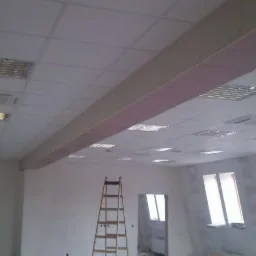 Montaż sufitu podwieszanego w pomieszczeniu biurowym, widoczna konstrukcja nośna i oświetlenie rastrowe.