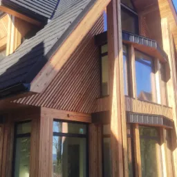 Nowoczesny dom z drewnianą elewacją w stylu góralskim, z dużymi oknami i ciemnym dachem. Charakterystyczne skośne deski i jasne drewno tworzą unikalny wygląd.