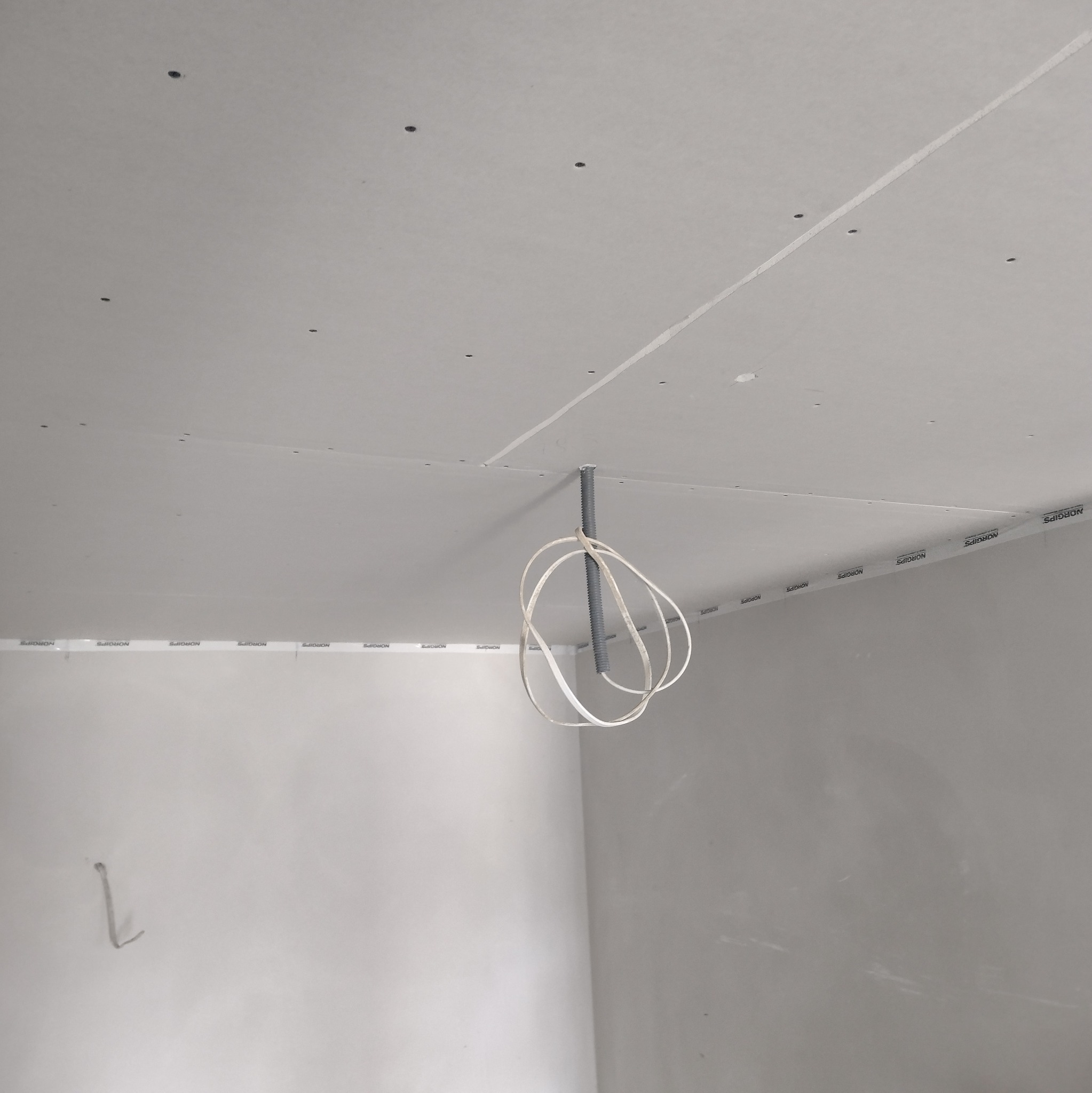 Montaż płyt karton-gips na suficie z widocznymi przewodami elektrycznymi. Widok z dołu, surowe wykończenie, taśma NORGIPS na łączeniach.