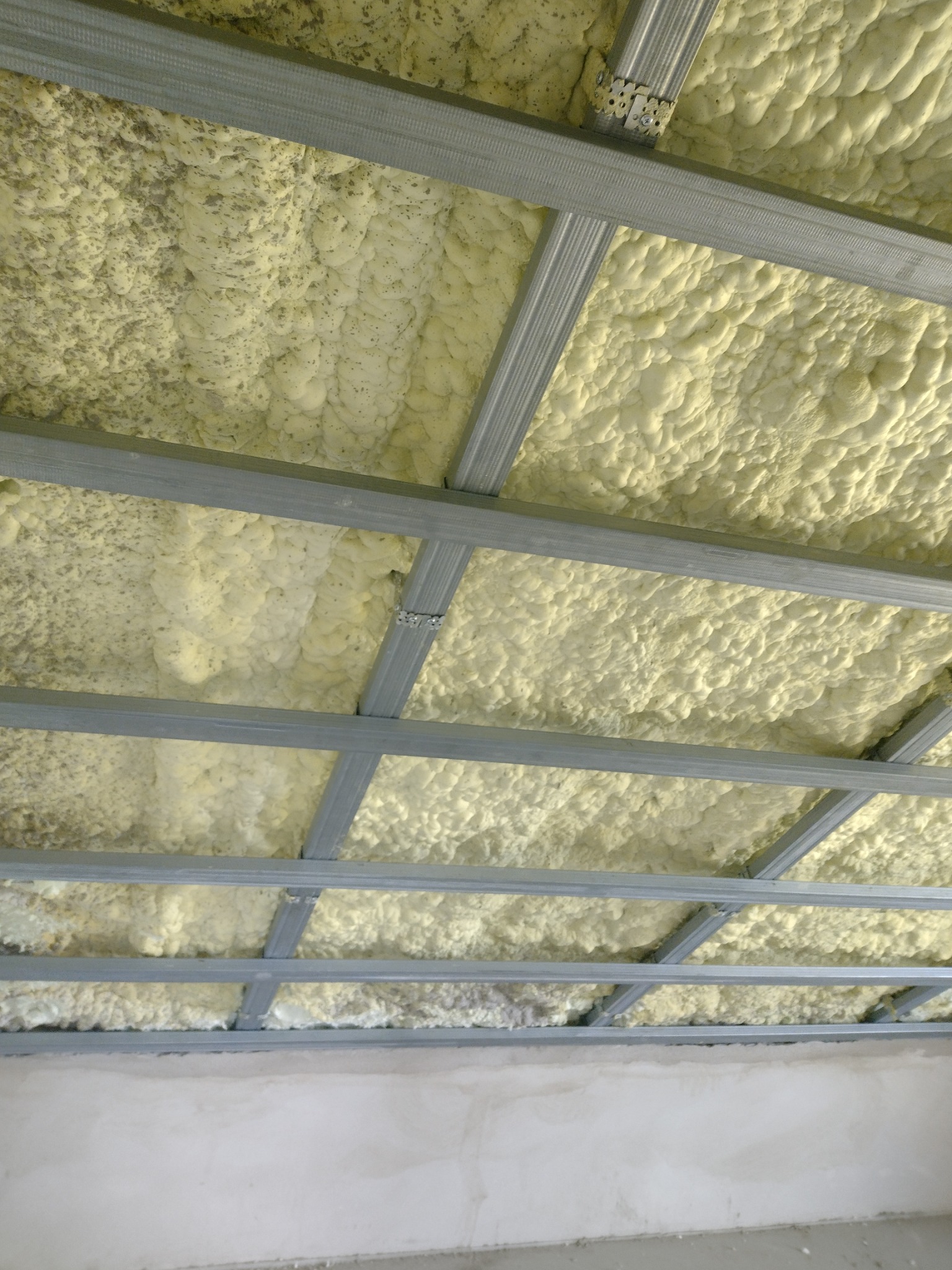 Ocieplenie poddasza pianką PUR widoczne między metalowymi profilami konstrukcyjnymi. Detal z bliska ukazuje strukturę piany i montaż profili.