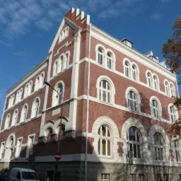 Elewacja odrestaurowanego, ceglanego budynku z białymi elementami dekoracyjnymi i łukowymi oknami. Widok na fasadę w jesiennym słońcu.