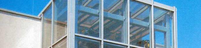 Szklana fasada budynku z widoczną stalową konstrukcją nośną i elementami wyposażenia wnętrza za szybami.