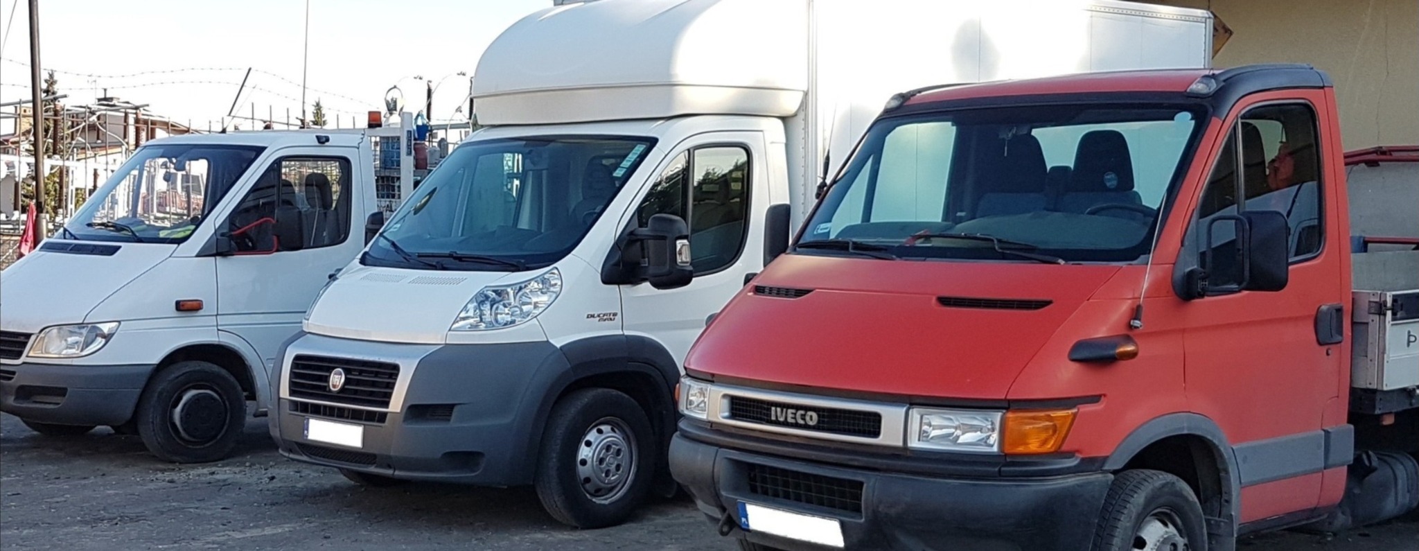 Trzy busy różnych marek (Mercedes Sprinter, Fiat Ducato, Iveco Daily) zaparkowane obok siebie na placu, widok z przodu.