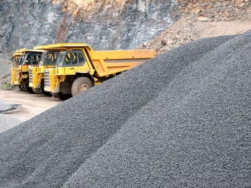 Hałda węgla typu orzech na tle dwóch żółtych wywrotek i skalistej ściany kamieniołomu.