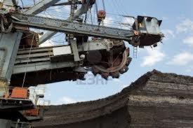 Ogromna koparka wielonaczyniowa wydobywa węgiel brunatny, widoczne warstwy geologiczne i fragment nieba z chmurami.