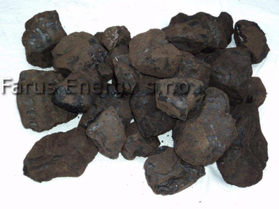 Kupa bryłek ekogroszku o nieregularnych kształtach, z widocznymi śladami pyłu węglowego, ułożona na białym materiale w słabym oświetleniu.