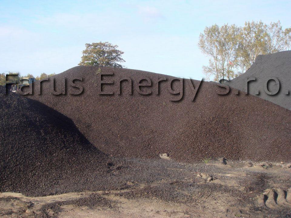 Góra miału węglowego z widocznym napisem 'arus Energy s.r.o.' na tle błękitnego nieba i drzew.