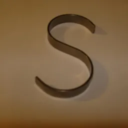 Metalowy haczyk w kształcie litery S na jasnym tle, rzucający cień.