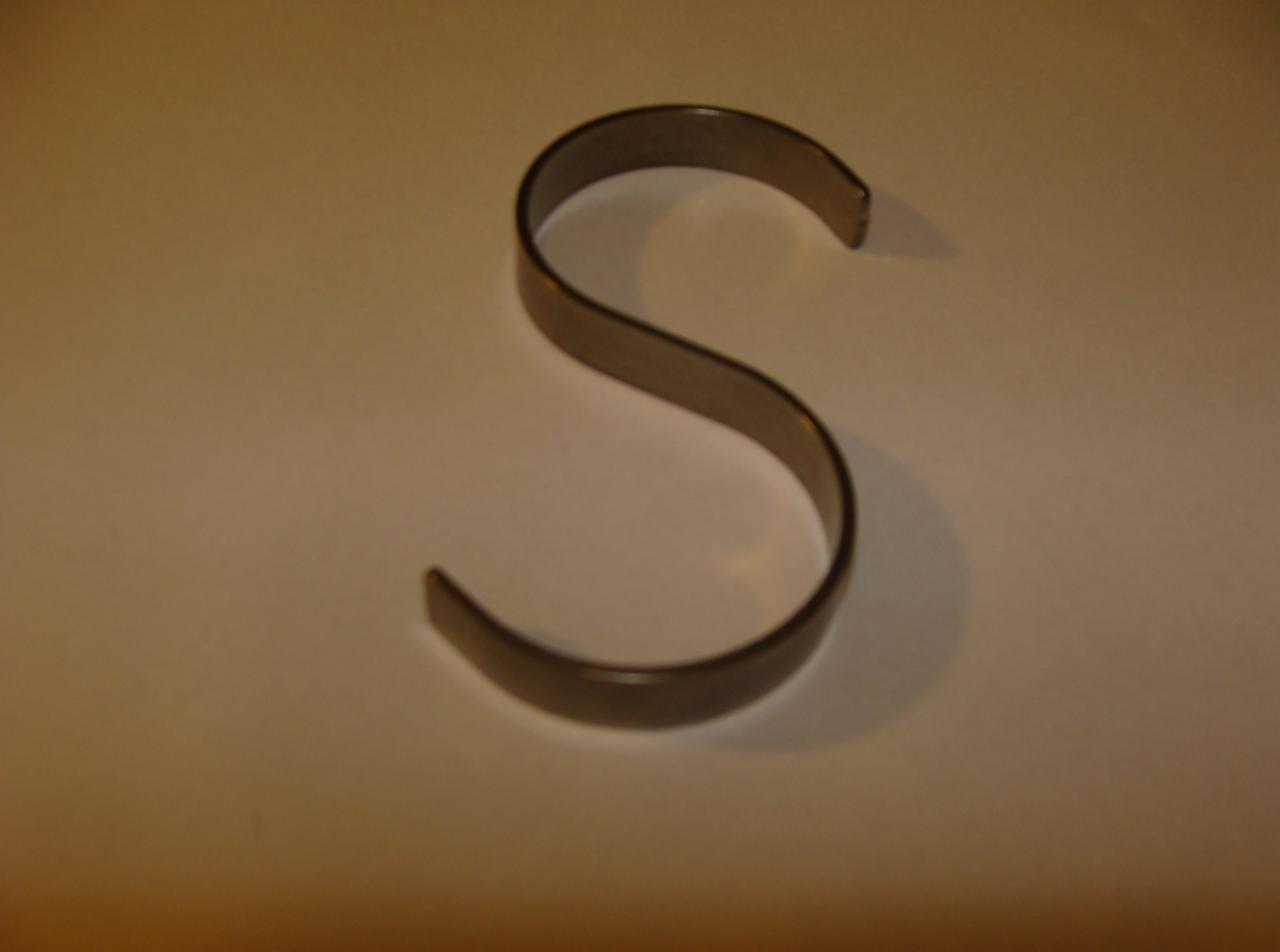 Metalowy haczyk w kształcie litery S na jasnym tle, rzucający cień.