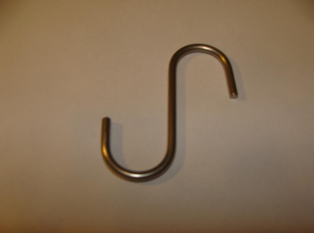 Metalowy haczyk w kształcie litery S, z zaokrąglonymi końcami, na jasnym tle. Prosty design, użyteczny w ogrodzie do podwieszania doniczek lub narzędzi.