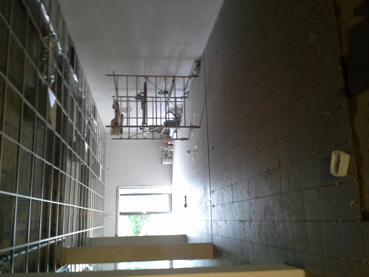 Wnętrze w trakcie prac wykończeniowych: metalowa konstrukcja ściany działowej, rusztowanie malarskie, okno i ściana z widocznymi punktami mocowań. Ujęcie z góry.