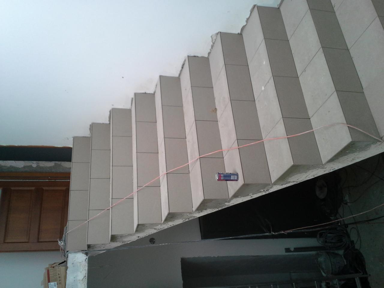 Wykończone płytkami schody żelbetowe w surowym wnętrzu, widoczne niedoskonałości i detale wykończeniowe, perspektywa od dołu.