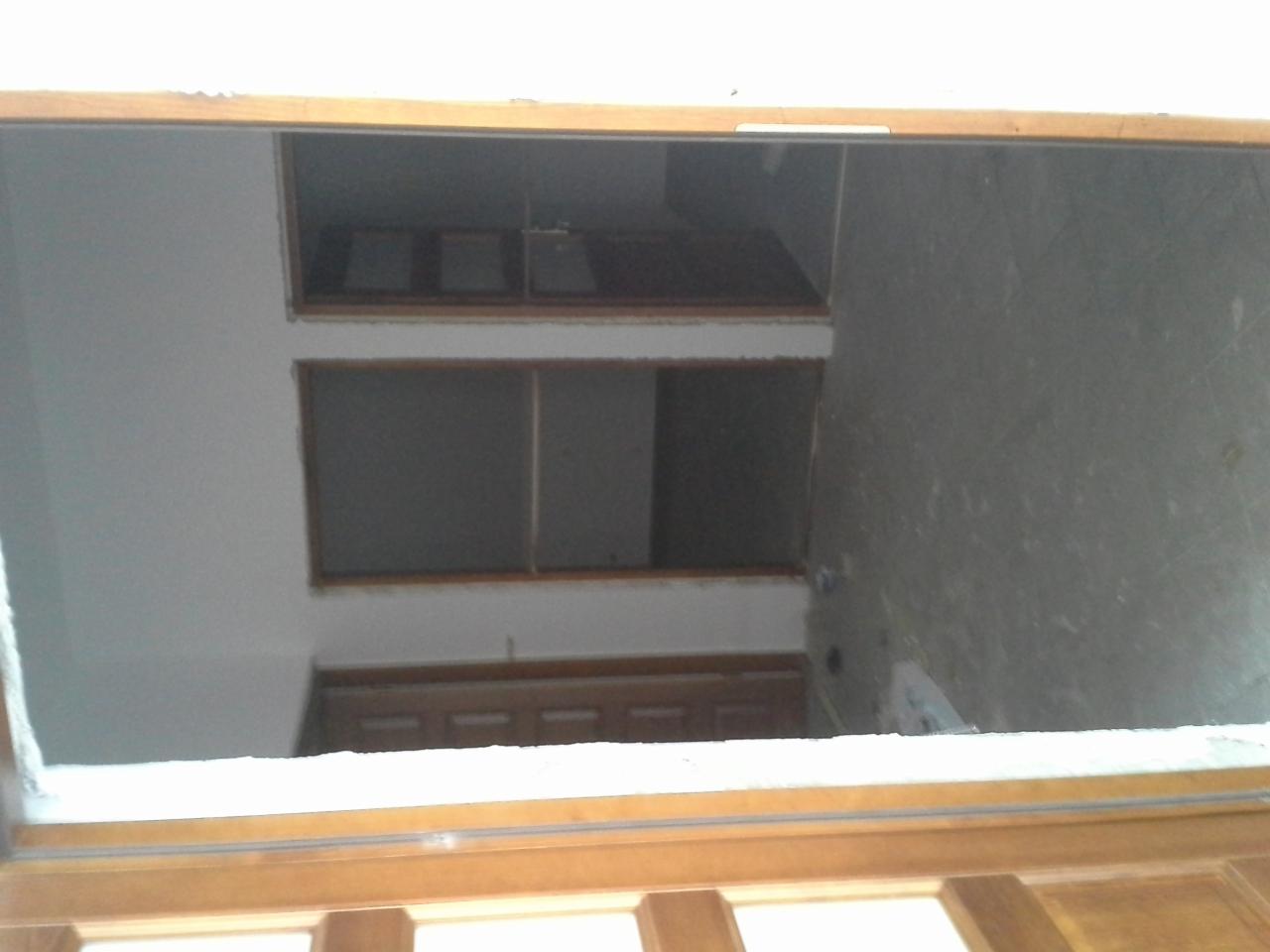 Wnętrze w trakcie remontu, widok przez drewnianą ramę okienną na surową ścianę i otwory okienne na różnych poziomach. Widoczne ślady po wyburzeniach.