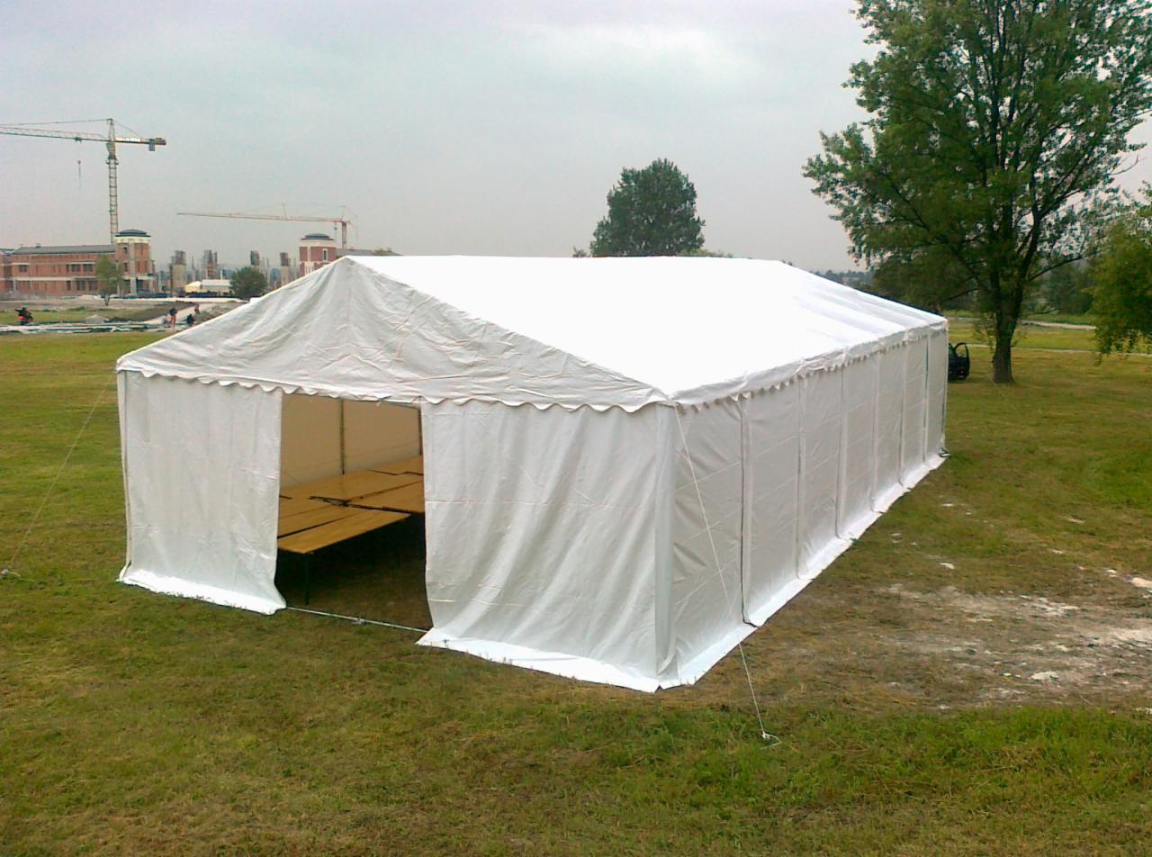 Biały namiot magazynowy z otwartym wejściem na trawiastym terenie, w tle budynki i żurawie budowlane.