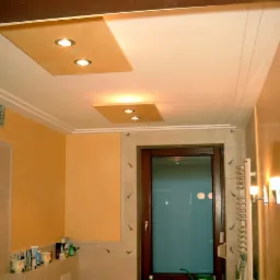 Jasna łazienka z kremowymi ścianami, podwieszanym sufitem z punktowym oświetleniem, grzejnikiem drabinkowym i oknem z ciemną ramą.