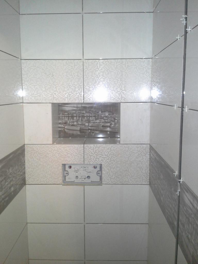 Wykończenie łazienki: ściany w jasnych płytkach z dekoracyjnym motywem portu, widoczne krzyżyki dystansowe, przygotowane miejsce na armaturę podtynkową.