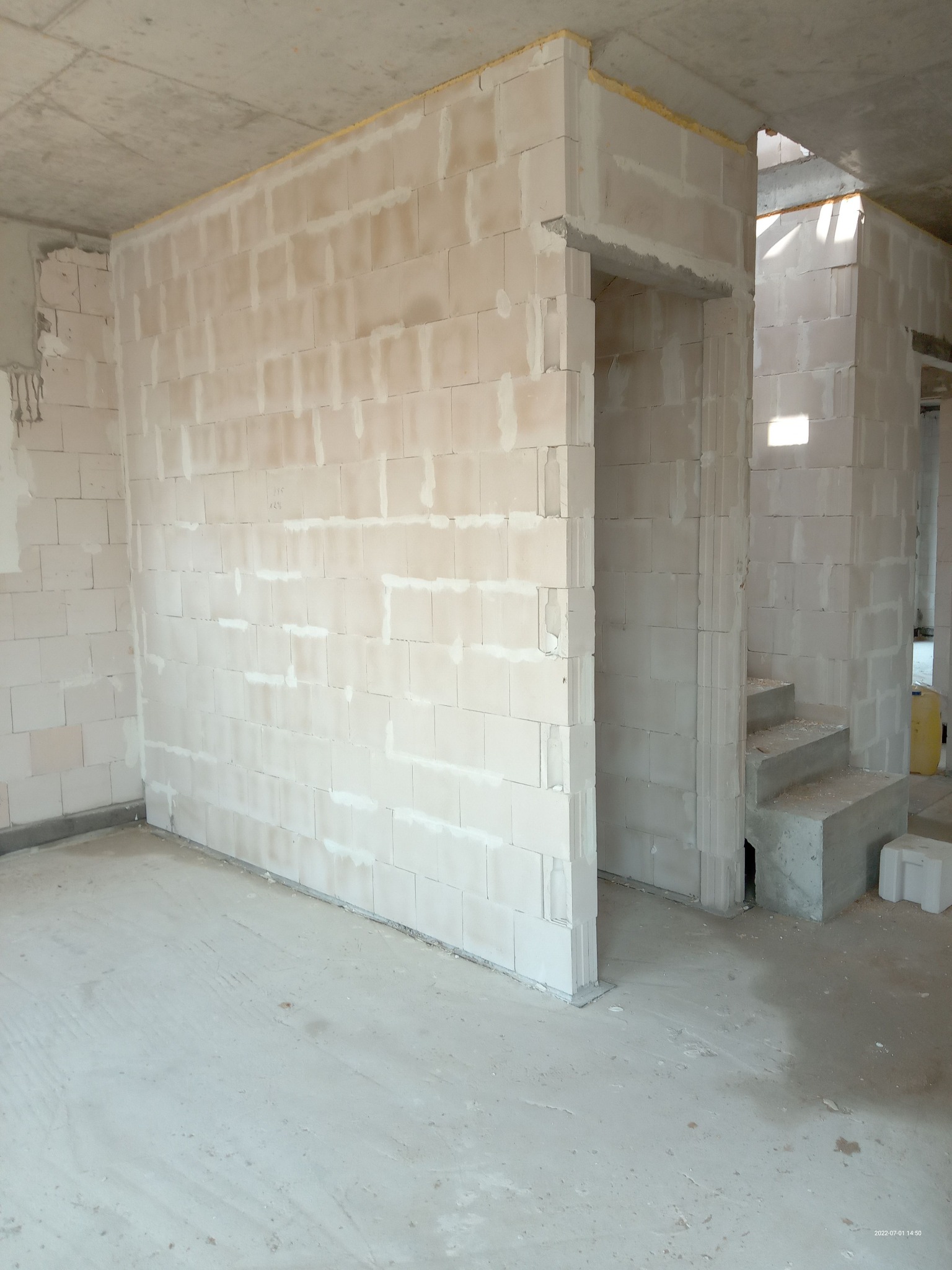 Surowe wnętrze w trakcie budowy: ściany z białych bloczków, betonowy strop, wstępne schody betonowe, widoczne złączenia i zaprawa, surowy beton na podłodze.