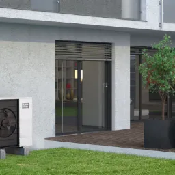 Nowoczesna pompa ciepła, model EcoDan, zamontowana na betonowych podstawach przy elewacji domu z dużymi przesuwnymi oknami i tarasem z drewnianą podłogą, na pierwszym planie trawnik i ozdobne...