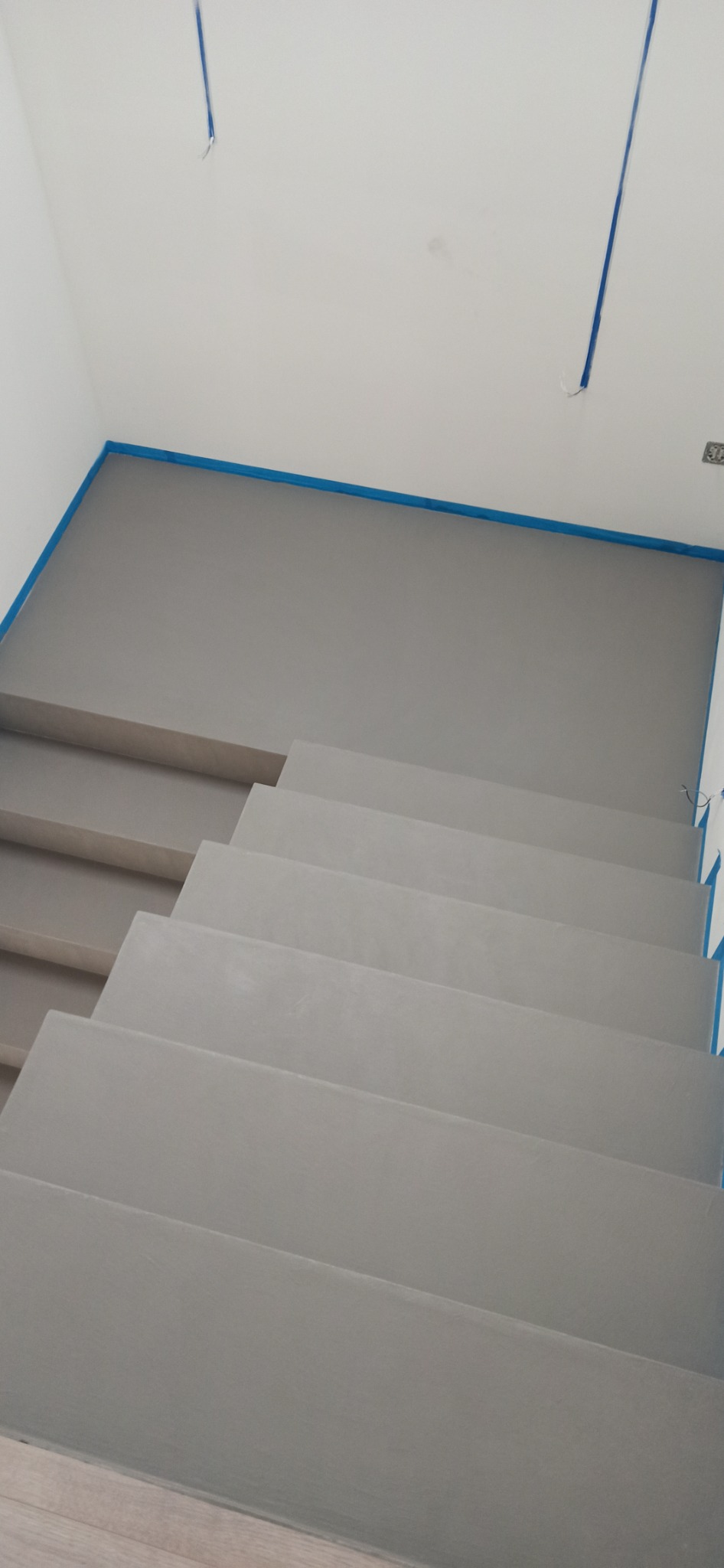 Wykończone schody wewnętrzne w szarości, zabezpieczone taśmą malarską przy ścianie i suficie, widok z góry.