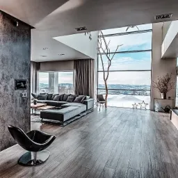 Przestronny salon z panoramicznym oknem, szary narożnik, designerski fotel i widok na zimowy krajobraz za oknem.