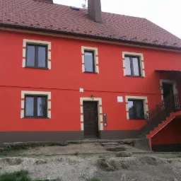 Pomarańczowy dom dwupiętrowy z brązowymi akcentami, kremowymi obramowaniami okien i drzwiami wejściowymi na podeście ze schodami.