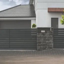 Nowoczesna, przesuwna brama wjazdowa w kolorze antracytu z poziomymi panelami, zamontowana w Suchym Dębie, z widocznym fragmentem ogrodzenia z siatki i kostką brukową na podjeździe.