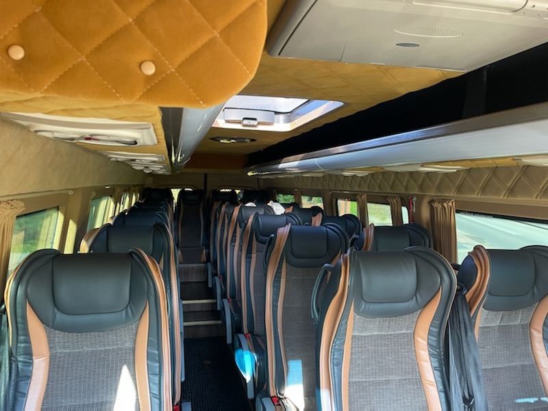 Wnętrze luksusowego autobusu z czarnymi skórzanymi siedzeniami z brązowymi akcentami i pikowanym, brązowym sufitem.