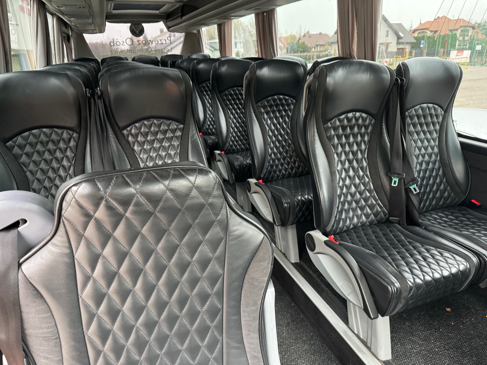 Wnętrze autobusu z rzędami czarnych, skórzanych foteli z pikowaniem w romby i szarymi wstawkami, widok z przodu pojazdu.