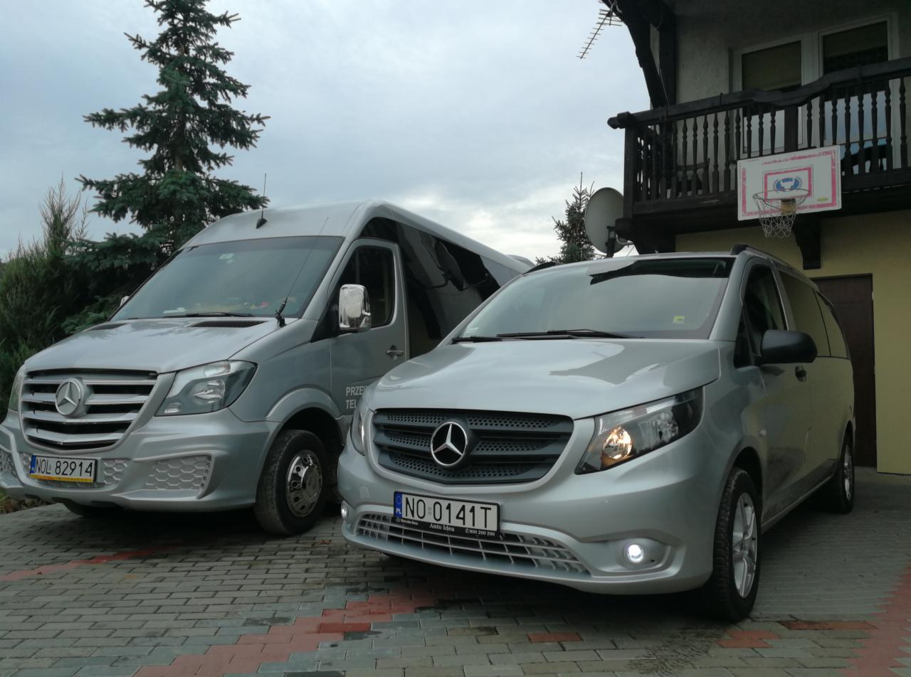 Dwa srebrne busy Mercedes-Benz zaparkowane na brukowanym podjeździe przed domem z balkonem i koszem do koszykówki.