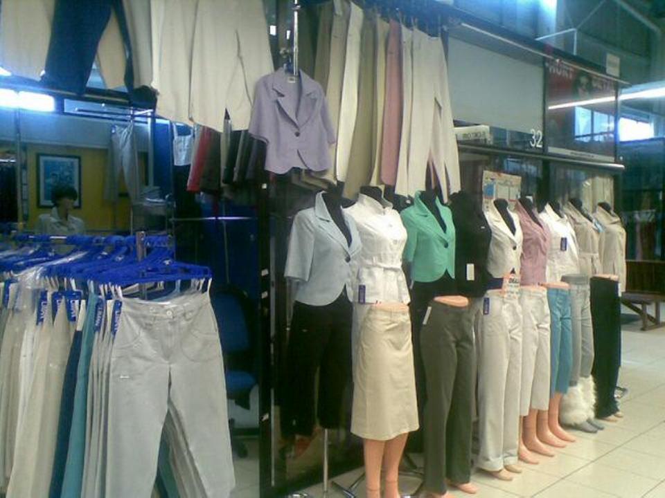 Wnętrze sklepu odzieżowego: rzędy ubrań damskich na wieszakach i manekinach prezentujących spodnie, spódnice i marynarki w różnych kolorach i fasonach.