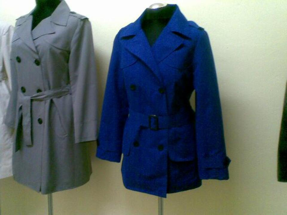 Dwa damskie płaszcze typu trencz: szary z wiązanym paskiem i niebieski z paskiem z klamrą, prezentowane na manekinach.